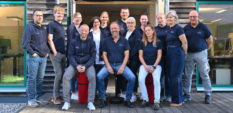 Gruppenfoto des Teams der ibag Seedorf vor dem Bürogebäude: Mehrere Mitarbeitende stehen und sitzen vor dem Eingang.